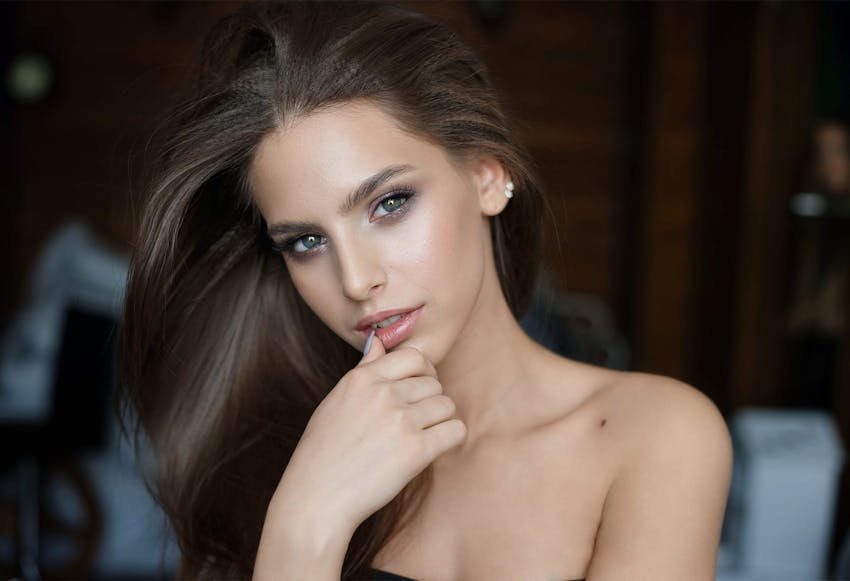 brunette model with a smokey eye makeup with her hand up to her mouth