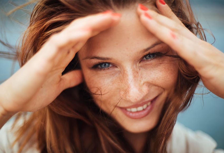 red-headed model smiling with her hands up at the top of her head