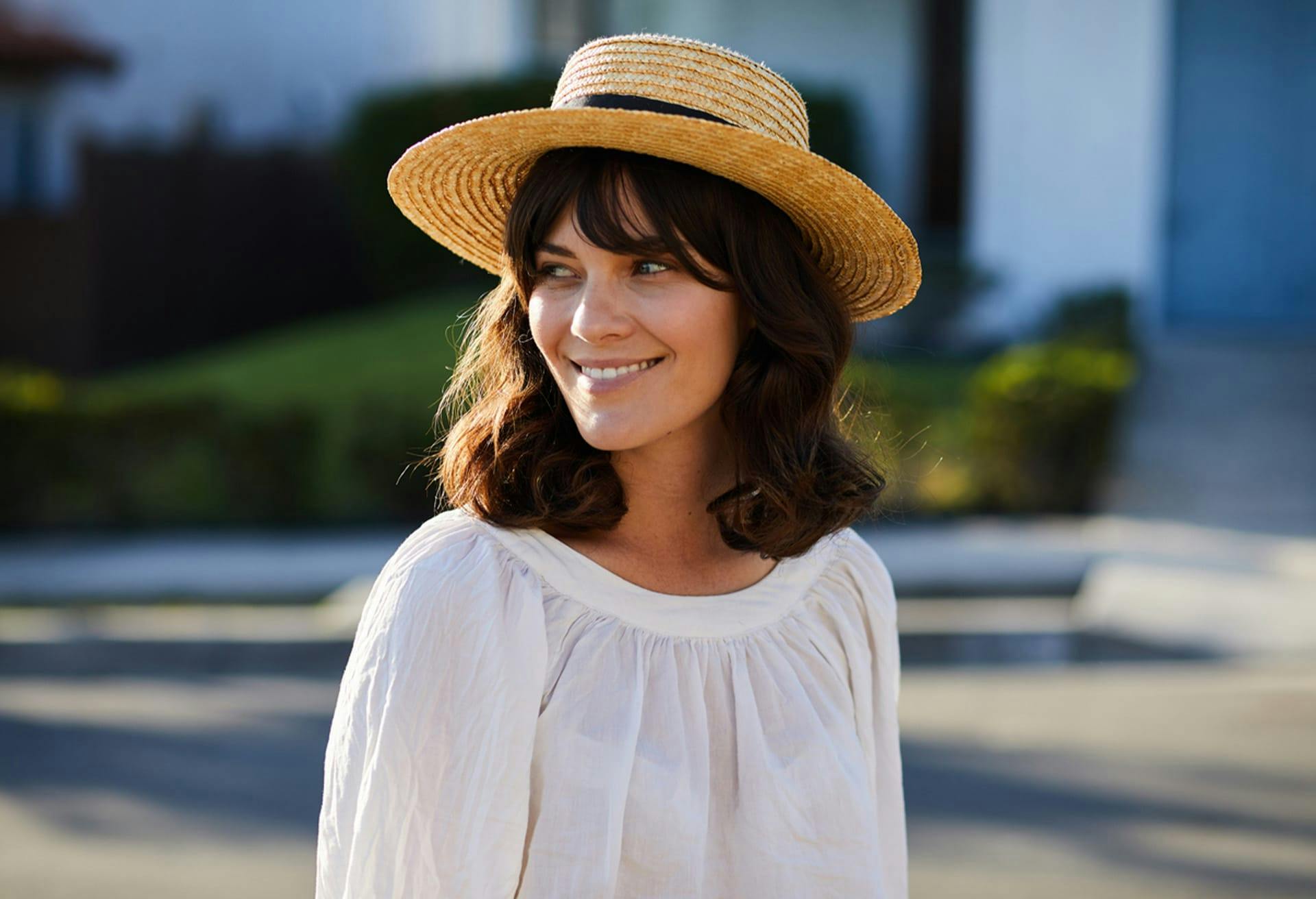 brunette woman outsite wearing a white shirt and a tan straw hat