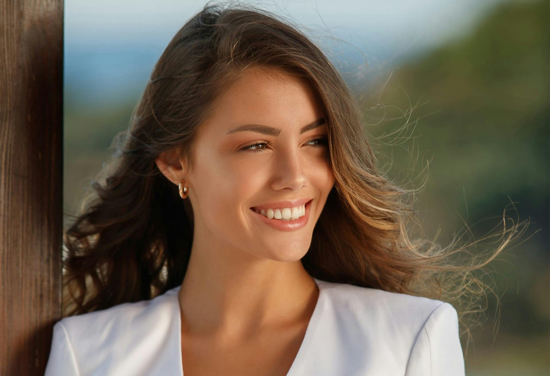 brunette woman looking off to the side of the camera smiling in a white blazer