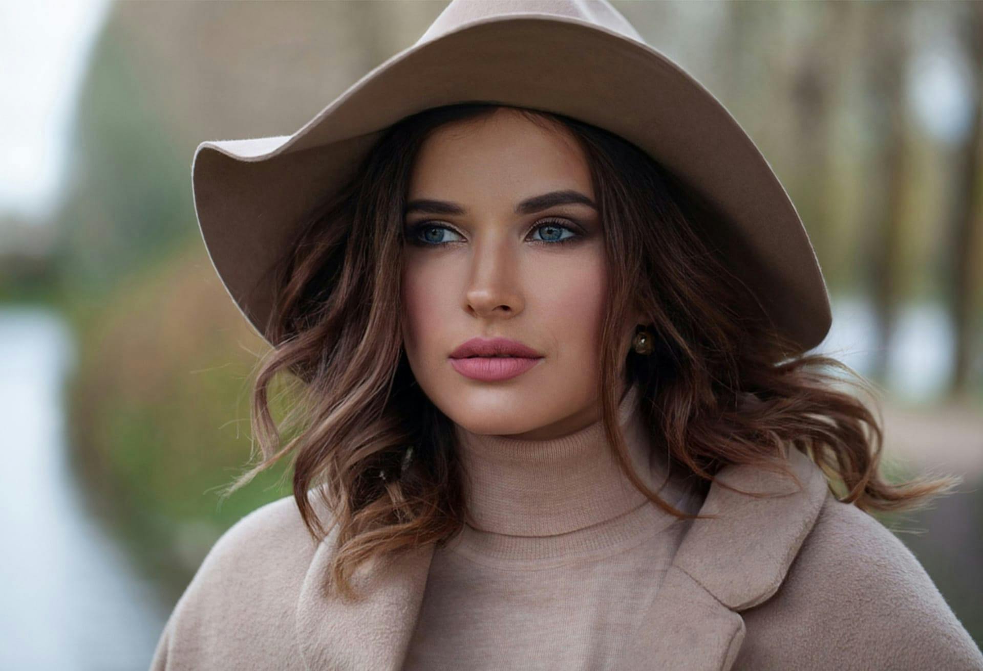 brunette woman with blue eyes in a tan turtle neck and jacket and brown hat