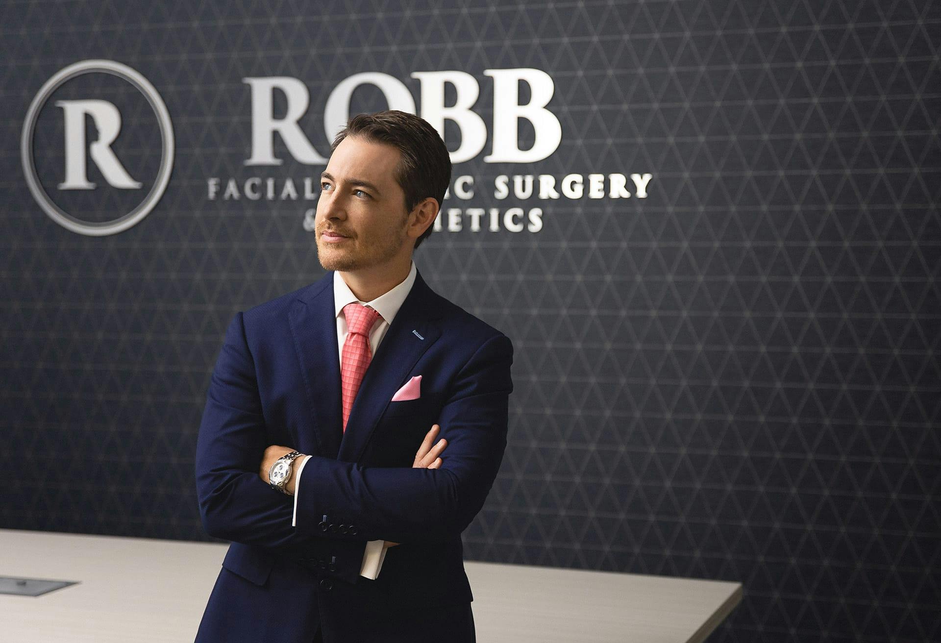 Dr. Robb standing in his lobby in a navy suit and pink tie