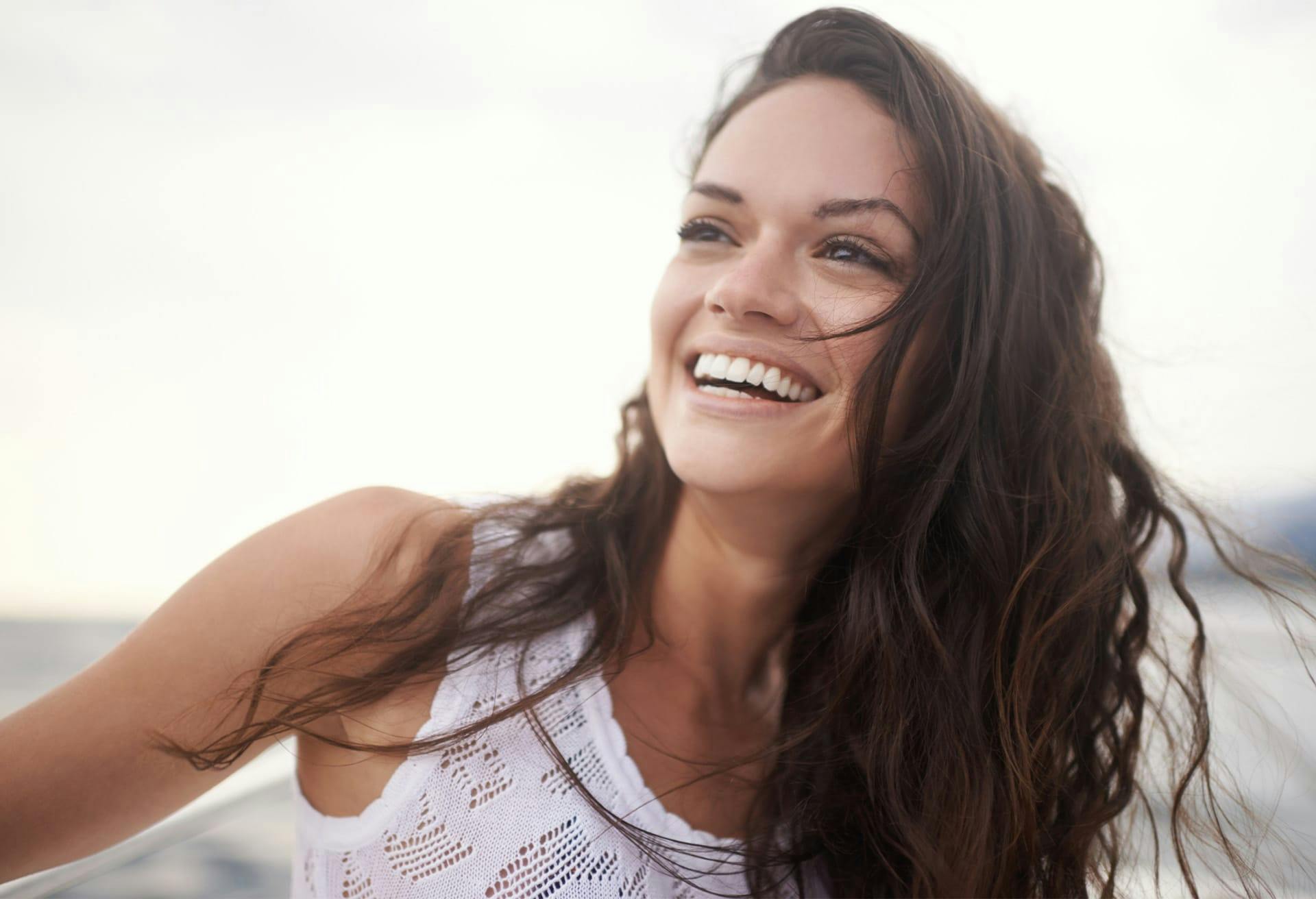 brunette woman smiling off to the side in a white tank top