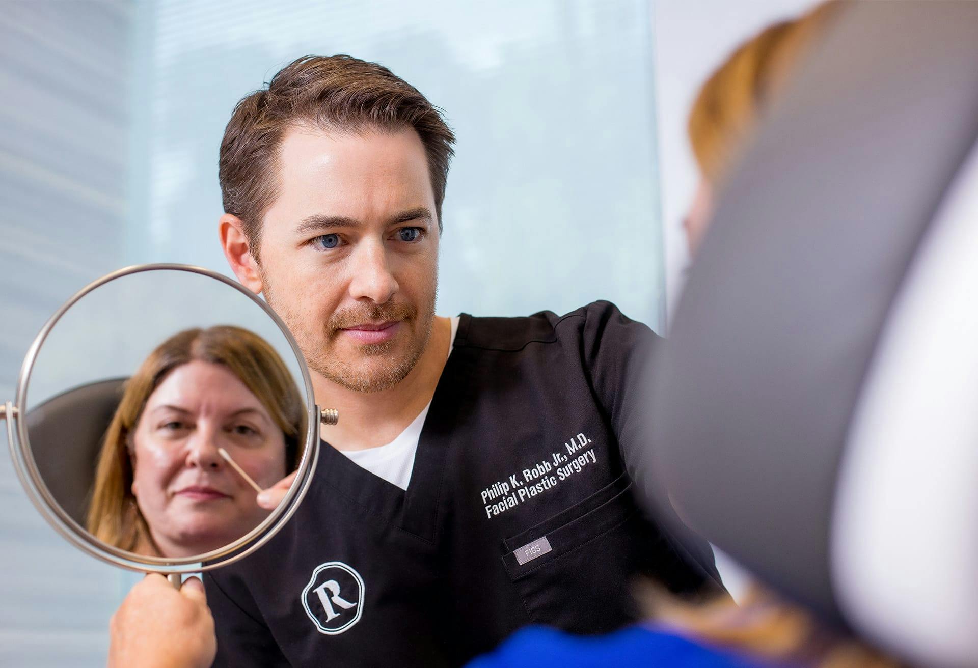 Woman looking in a mirror while being helped by Dr. Robb.