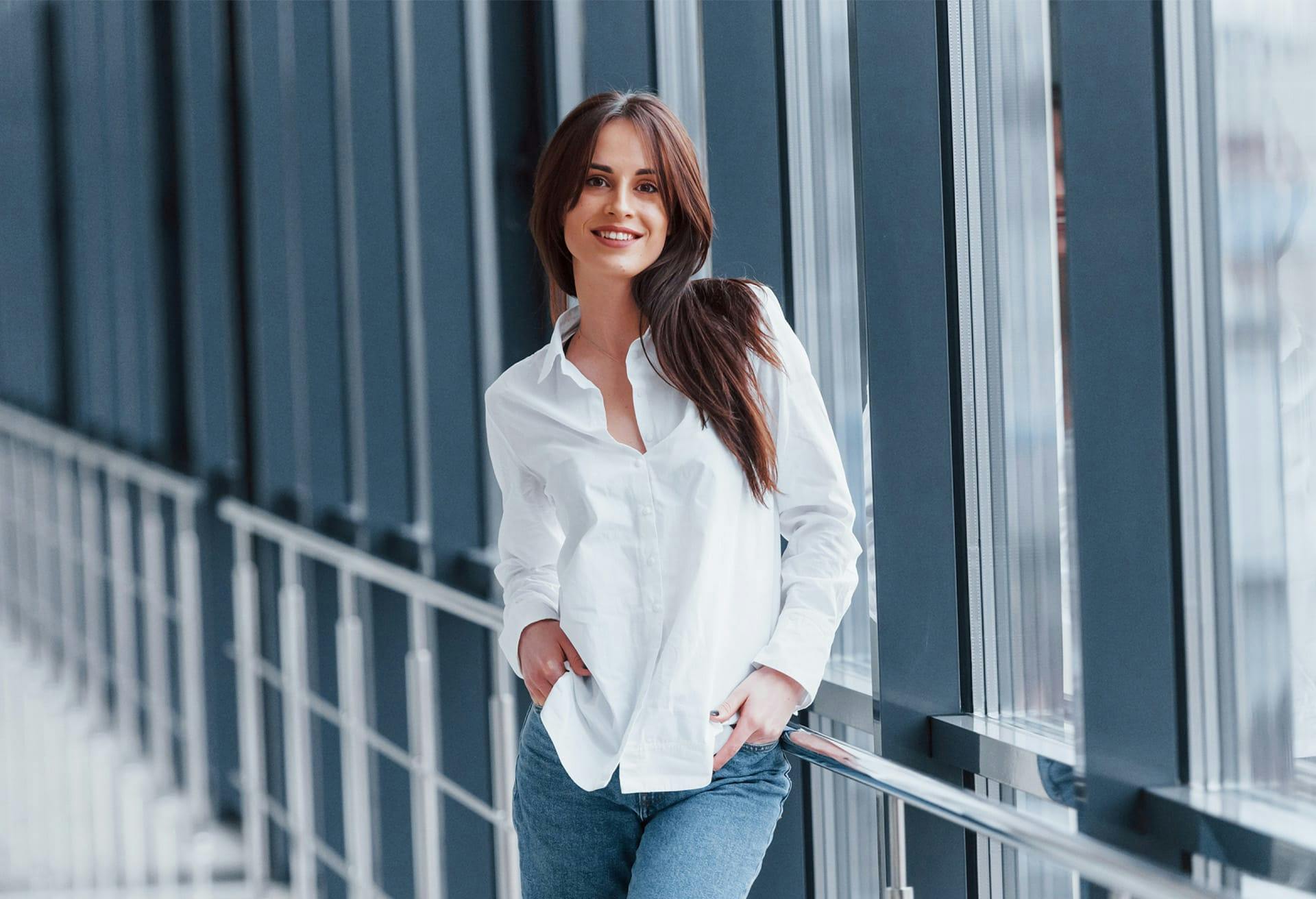 brunette woman standing in a hallway in a white button down and blue jeans