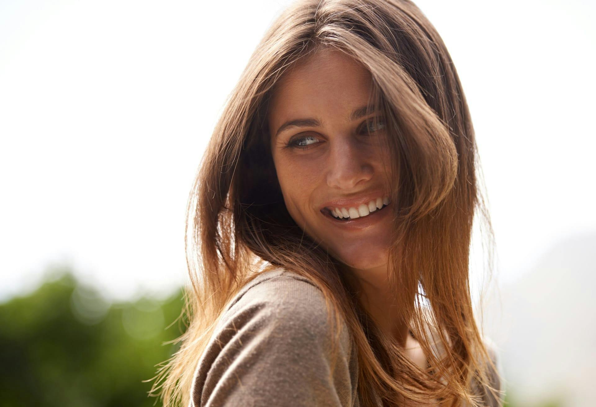 smiling brunette woman standing outside in a brown sweater