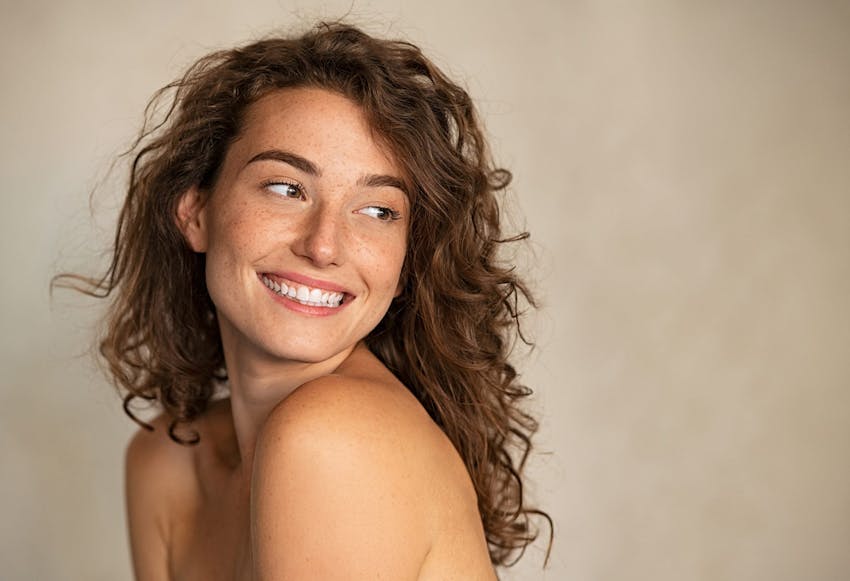 brunette woman with freckles looking over her shoulder