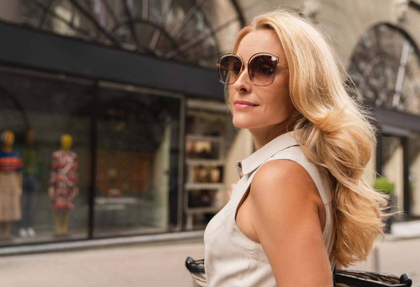 blonde woman walking on the sidewalk in sunglasses and a tan tank top