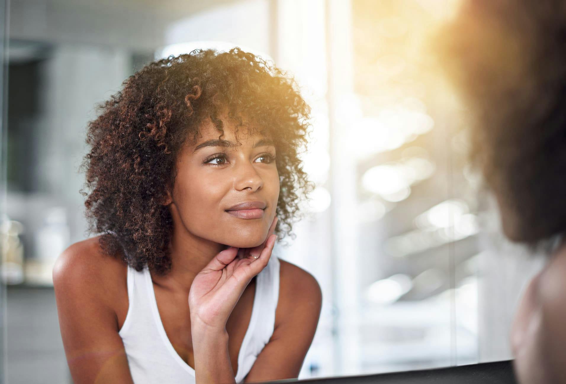 woman smiling and touching face in mirror