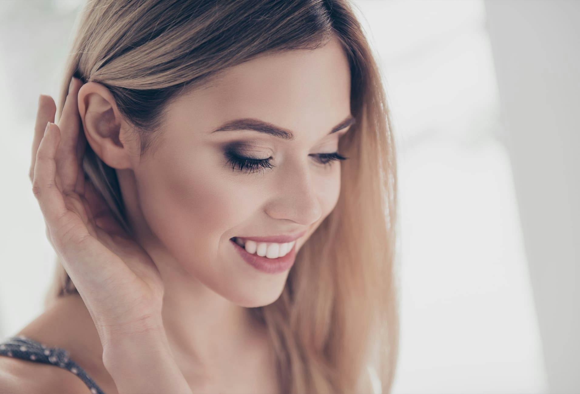 Woman smiling, looking down and pulling hair around ear