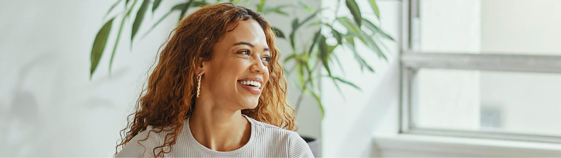 Woman smiling and sitting in front of plant and window