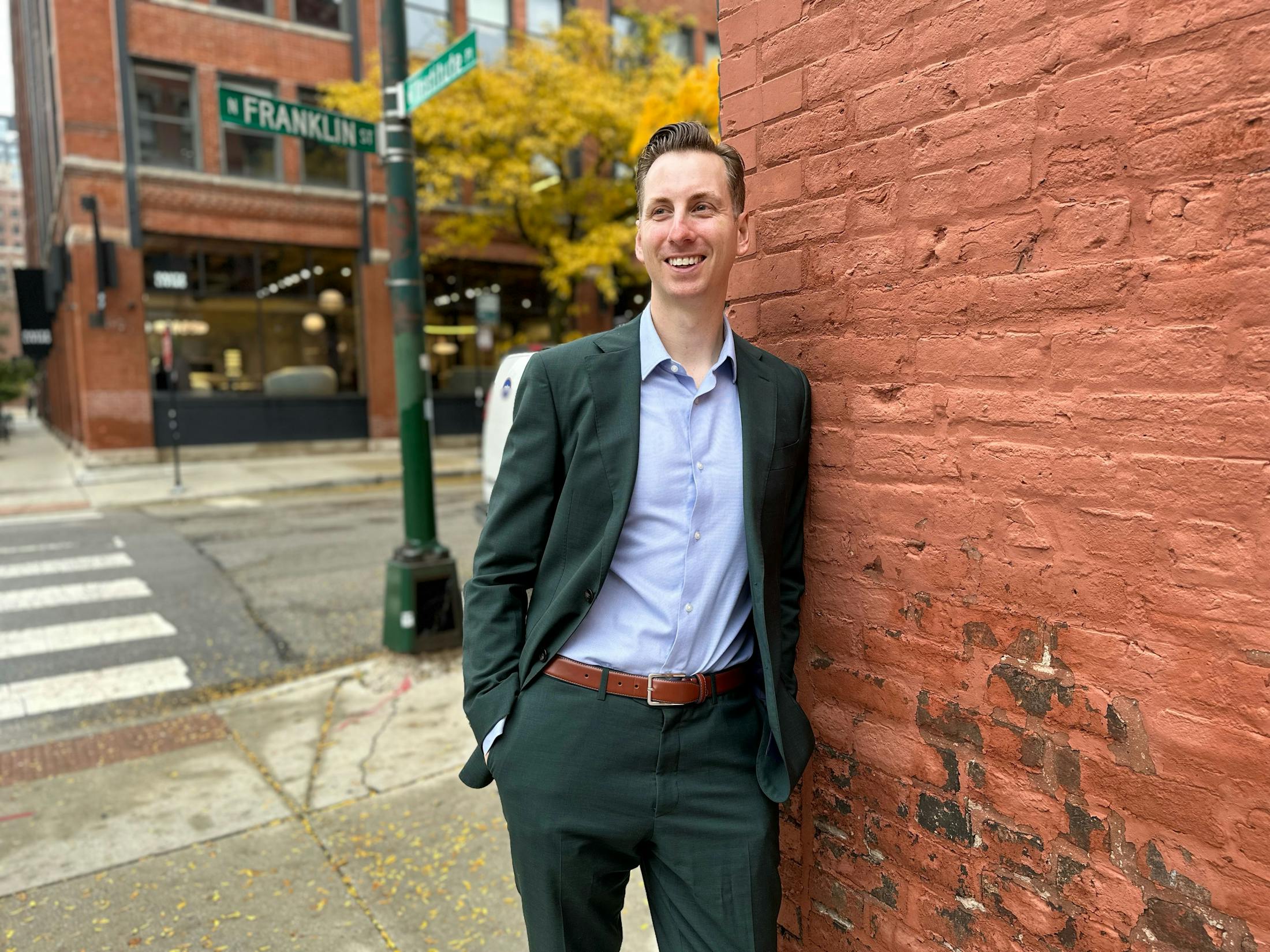 man leaning against a brick wall in a suit