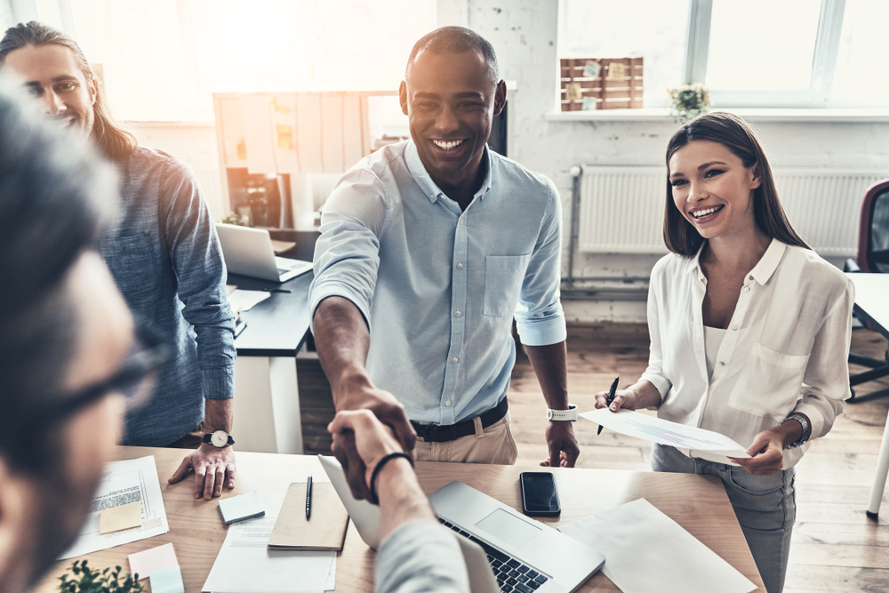 Motivated office workers shaking hands and meeting around a desk to discuss sales performance incentives.