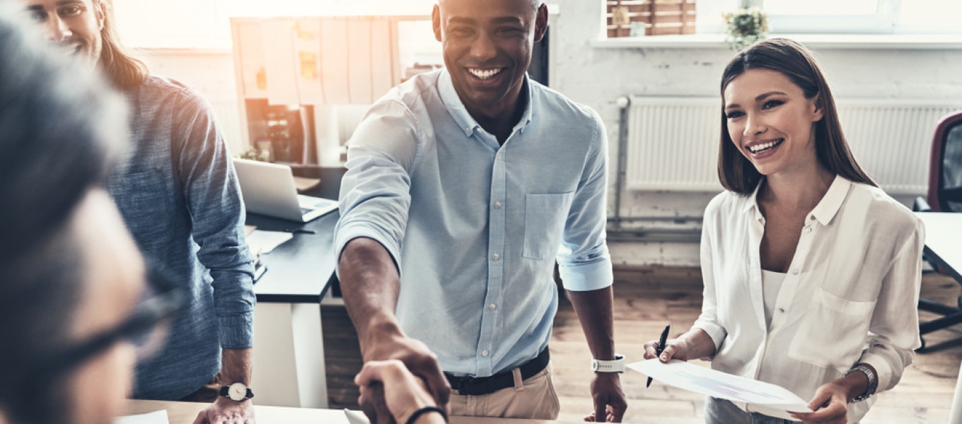 Motivated office workers shaking hands and meeting around a desk to discuss sales performance incentives.