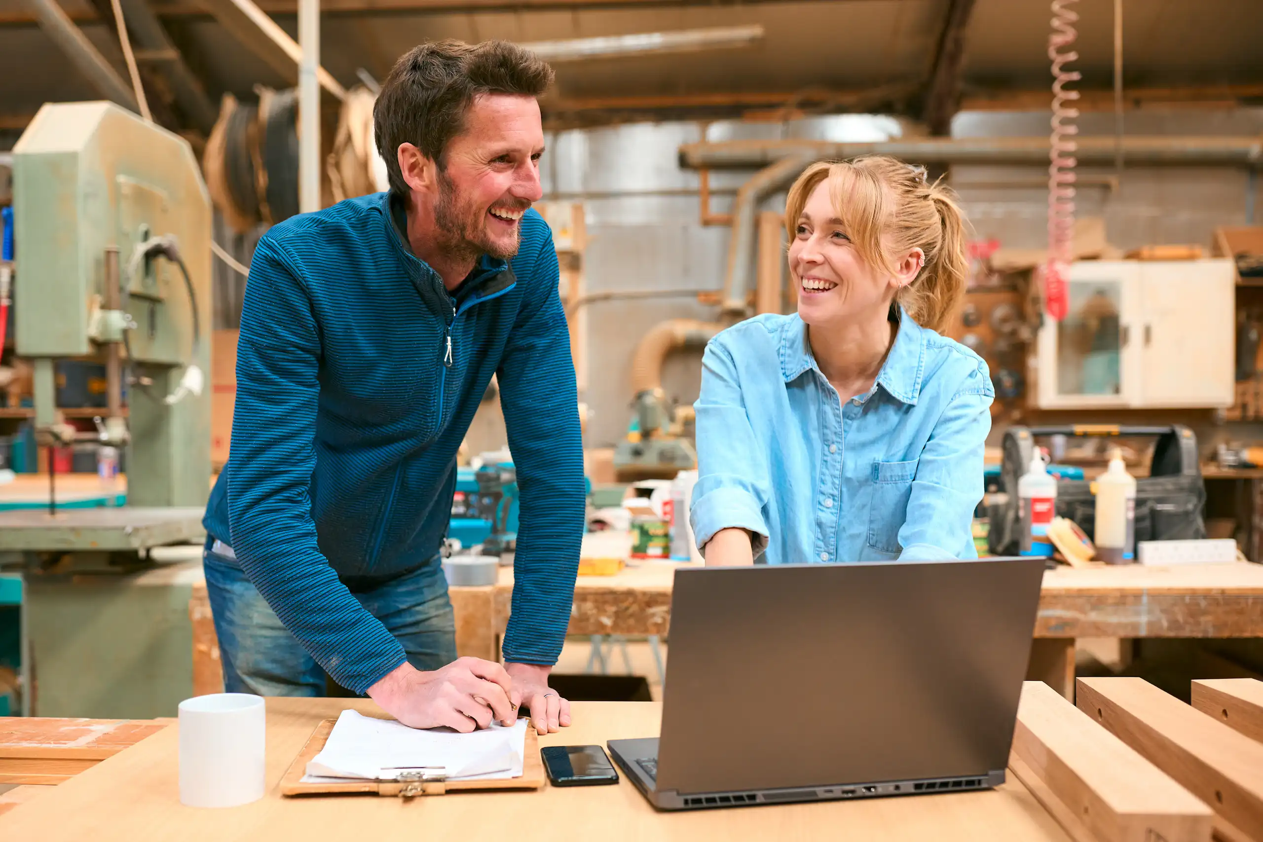 Two people working together at a laptop in a small workshop.