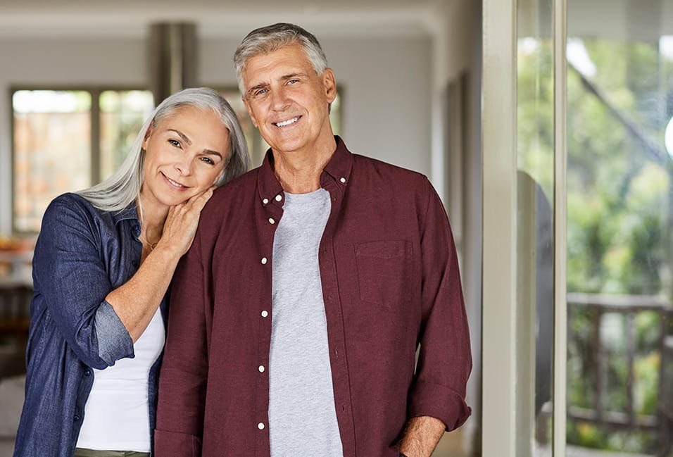 smiling older couple standing in front of a door in a house