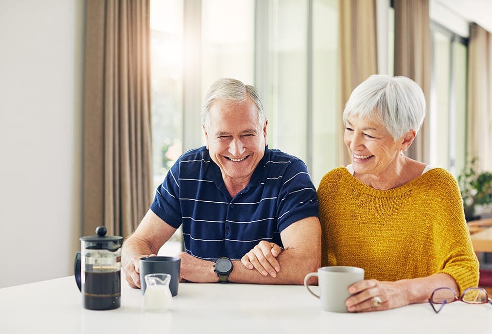smiling older couple sitting at a table with coffee cups