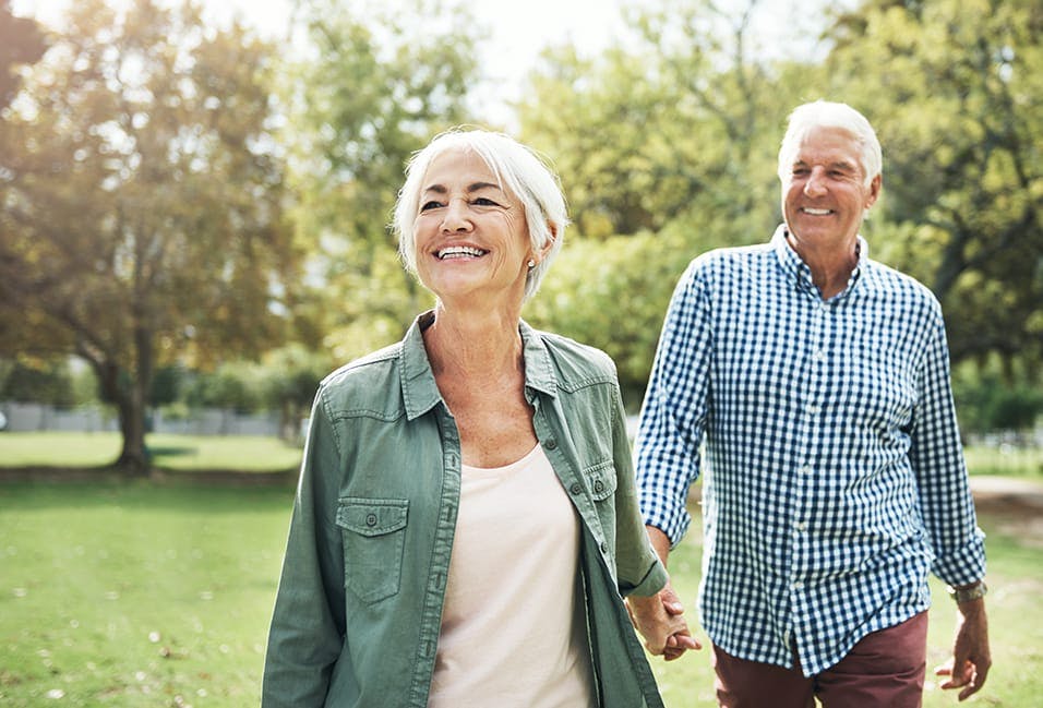 older couple walking in park holding hands and smiling
