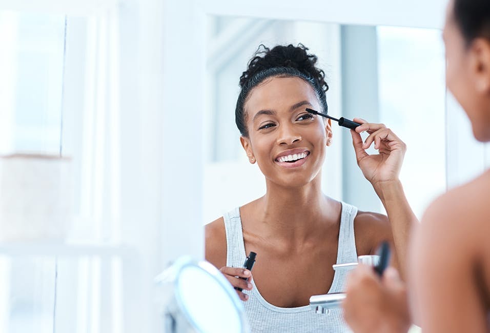 Woman applying mascara to her eyelashes while looking in the mirror