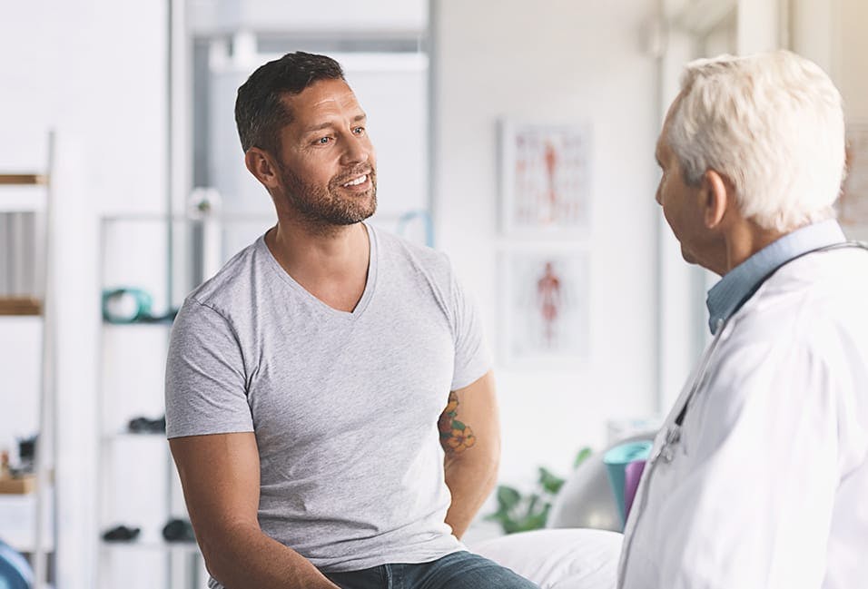 Man sitting on an exam table while taking with a physician