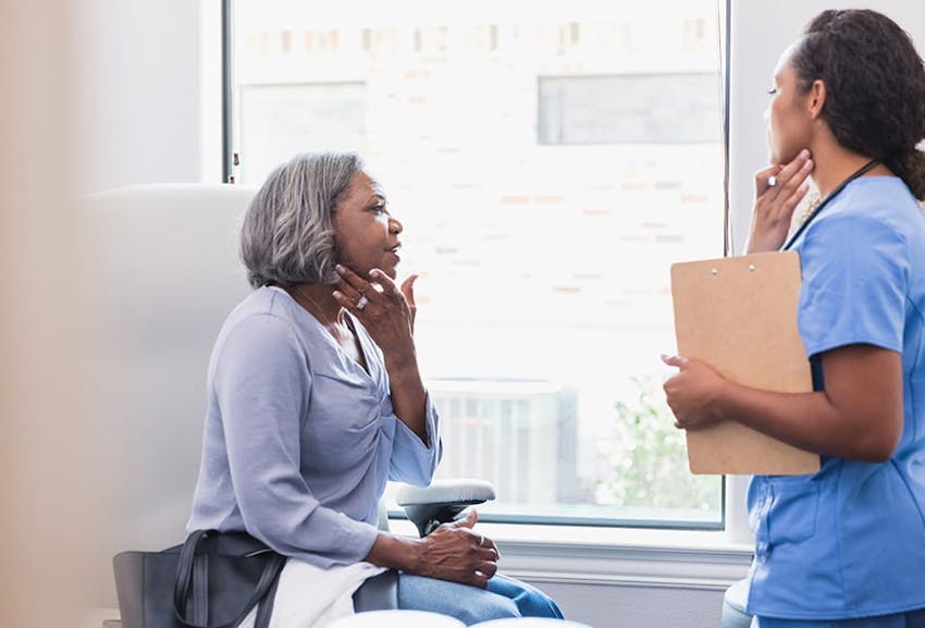 Physician meeting with an elderly patient and indicating a spot on their neck