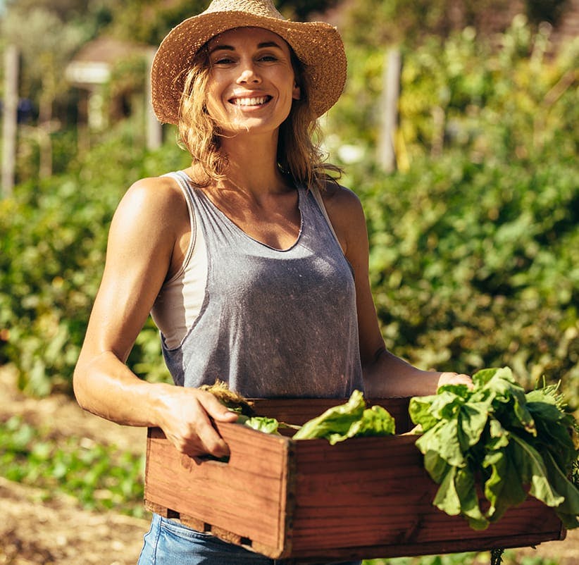 woman holding a crate of vegetables in a garden