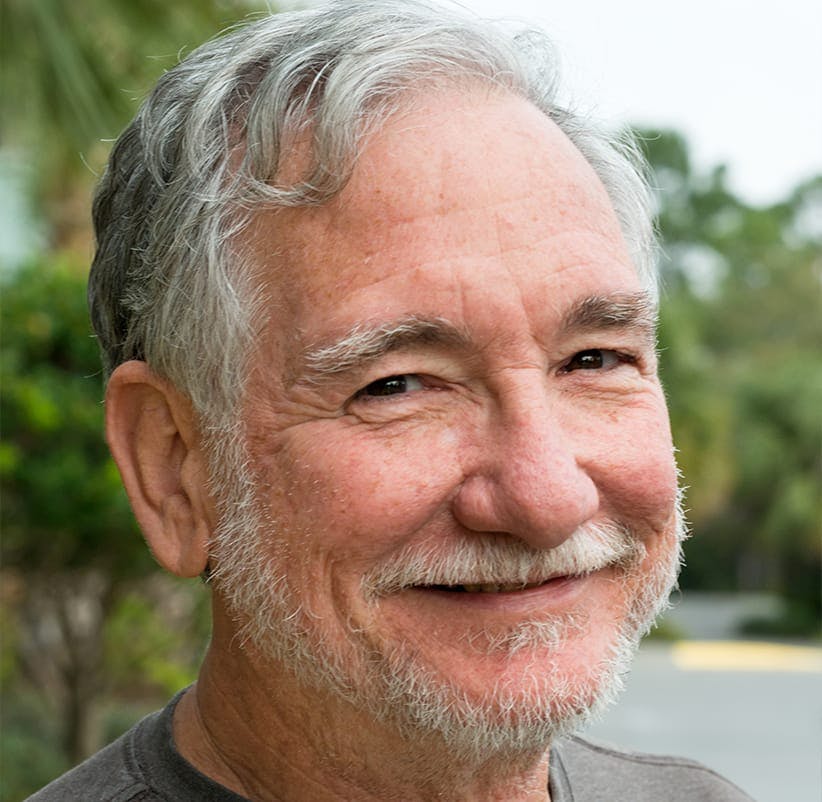 smiling man with gray hair and a mustache in a park