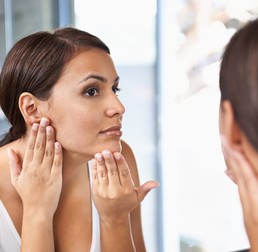 woman looking in mirror at her skin