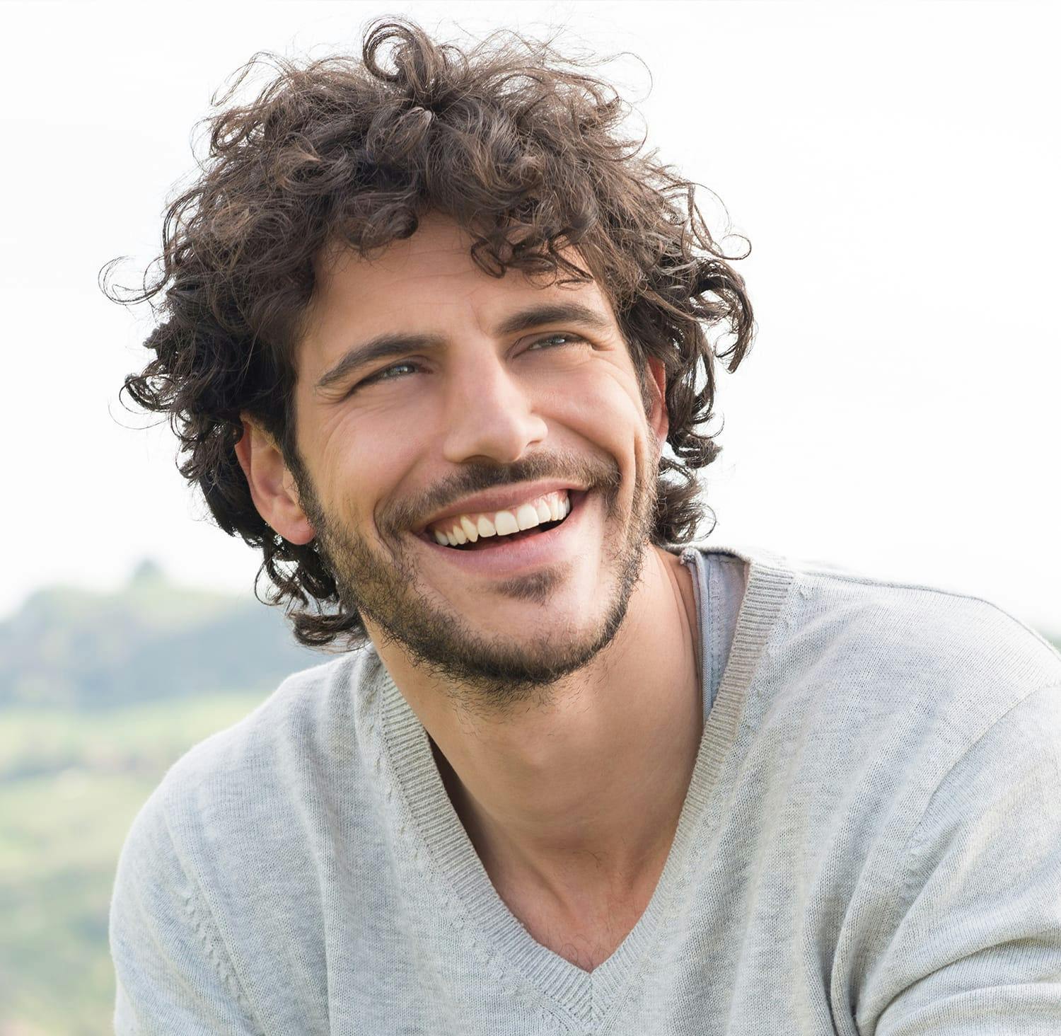 smiling man with curly hair and beard sitting on a hill