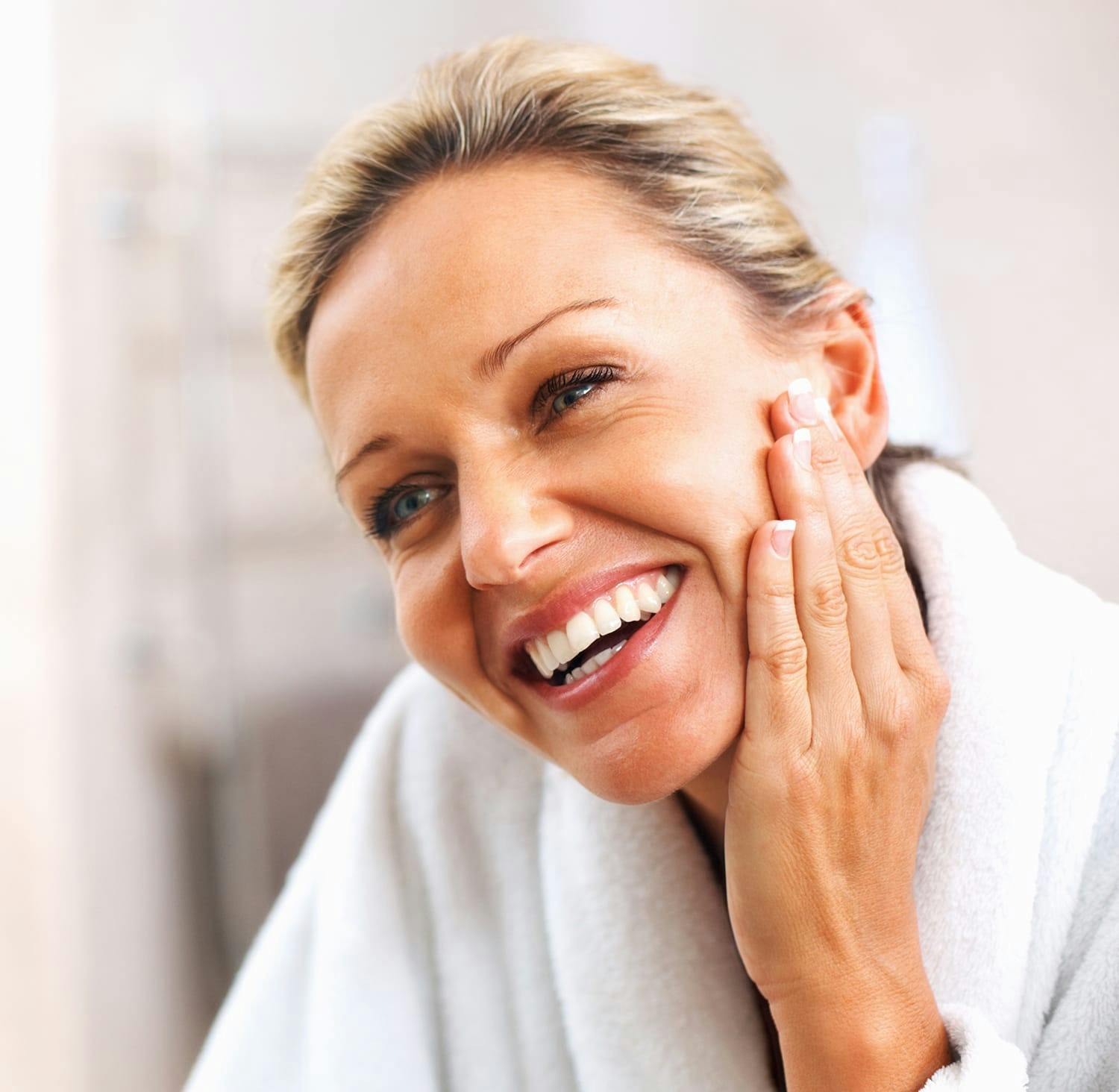 smiling woman in bathrobe looking at mirror with hand on face