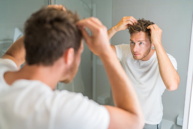 Brown-haired man looking at his hair in the mirror