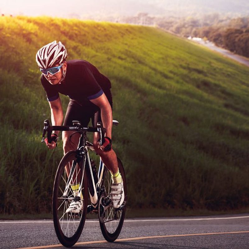 man riding a bike on a road with a grassy hill in the background