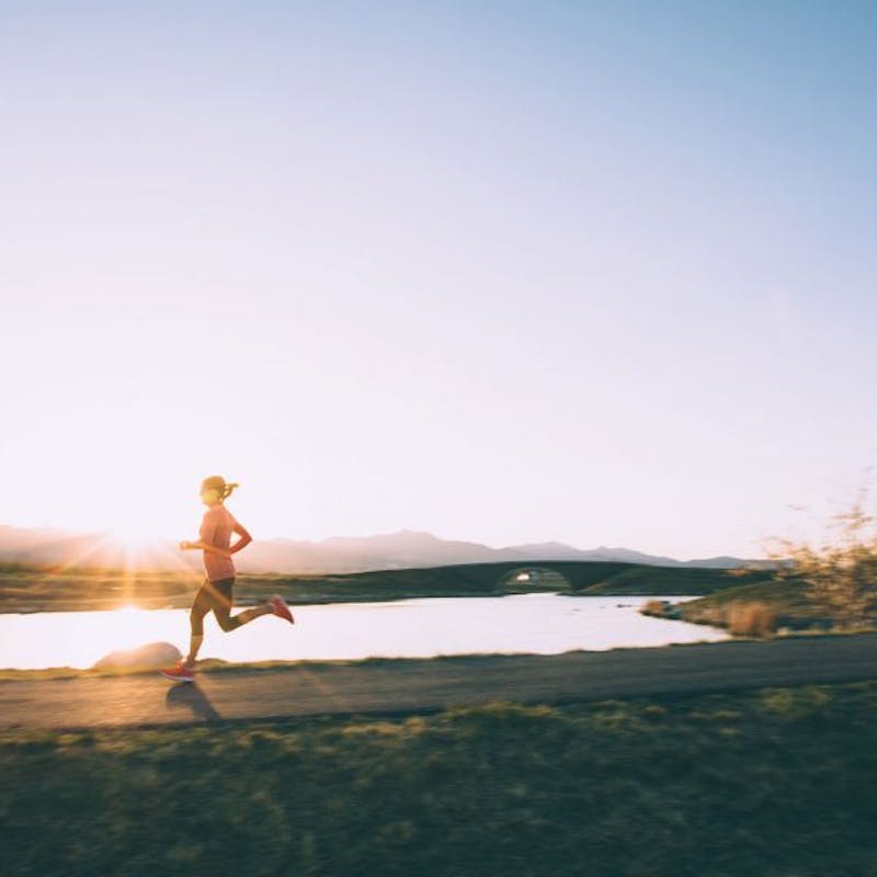 woman running on a road near a lake at sunset