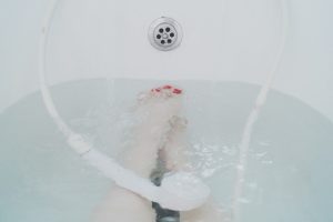 woman's legs in tub with water and shower head