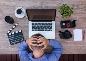 man with hands on head in front of laptop