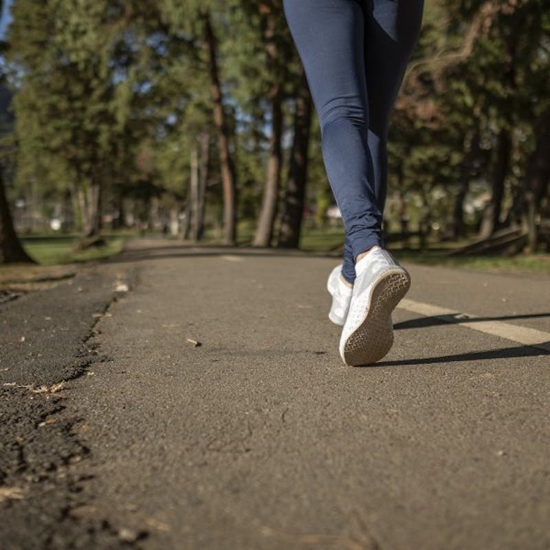 close up of feet walking on a paved path in a park with trees