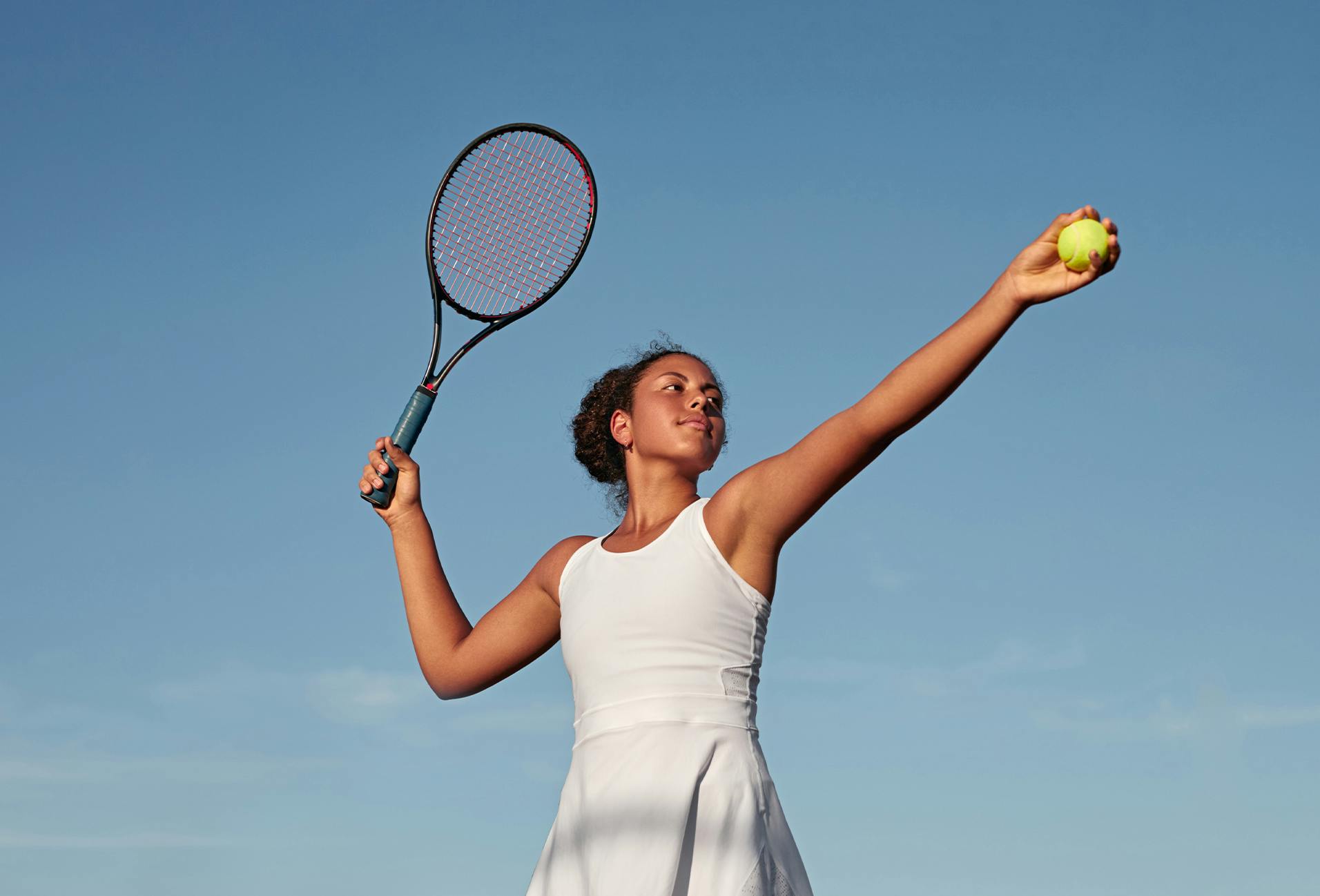 woman in white dress holding tennis racket and ball in air
