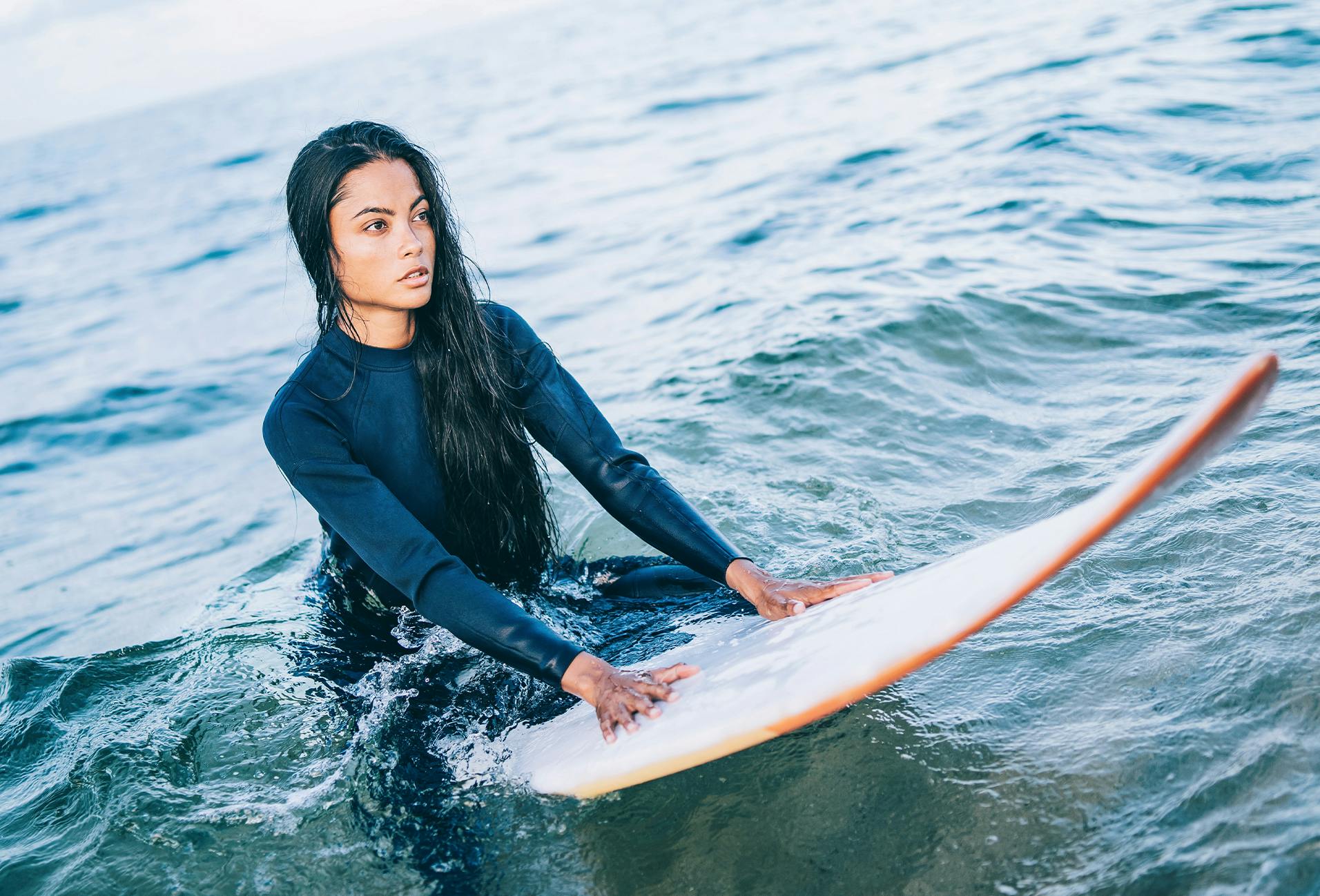 surfer in a wet suit sitting on a surfboard in the ocean