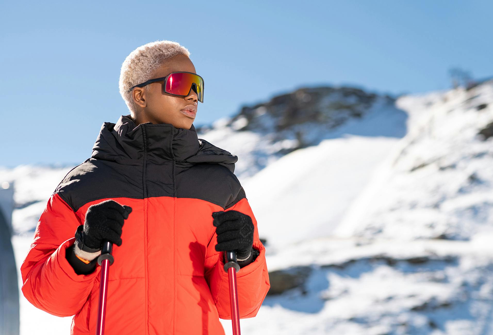 skier in red and black jacket standing on snowy slope with mountains in background