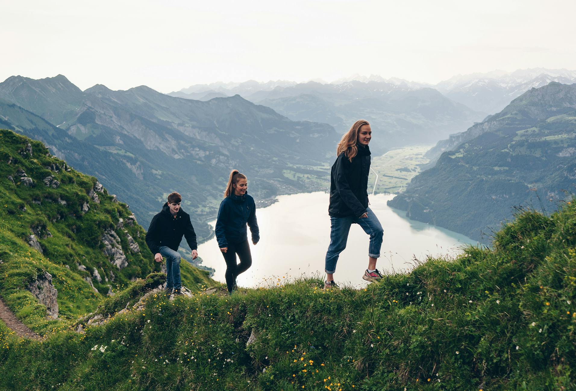 three people walking up a hill with a lake in the background
