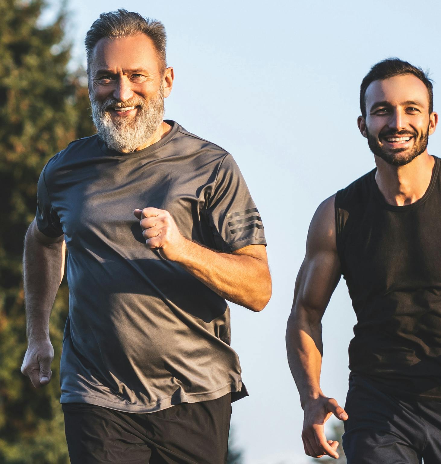 there are two men running together in a park with trees in the background