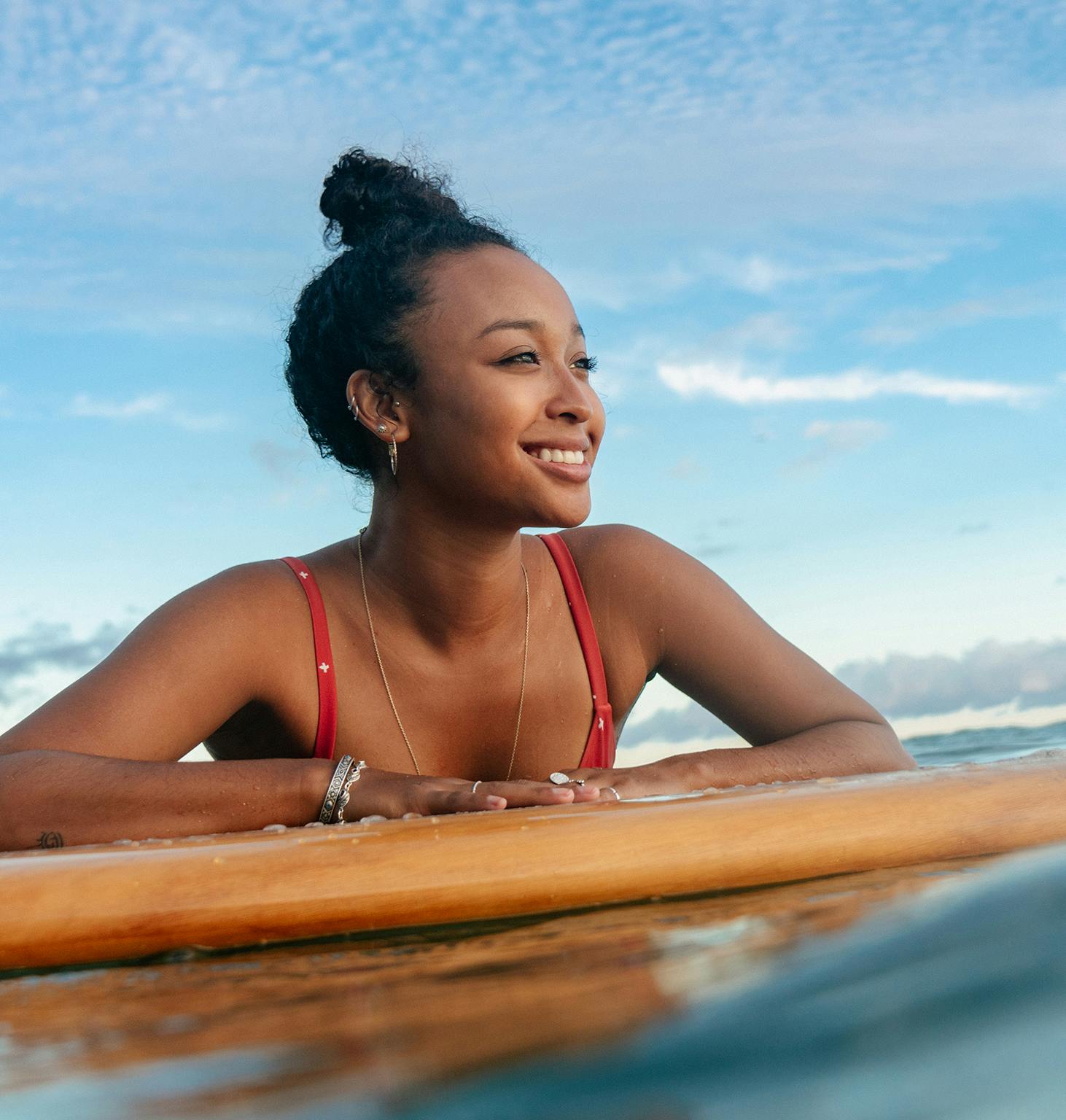 smiling woman in red bikini laying on surfboard in the ocean
