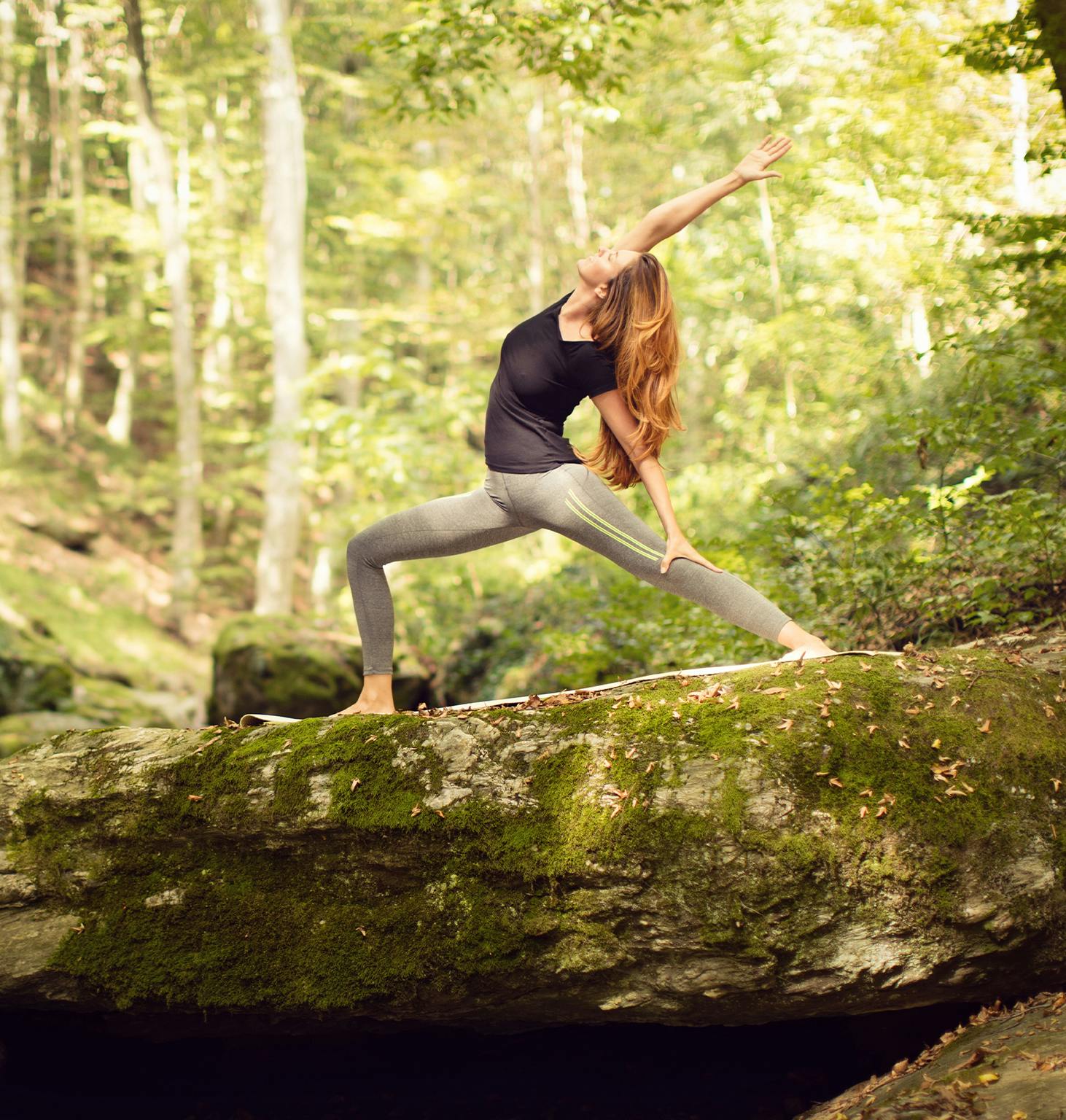 woman in a black top and grey pants doing yoga on a rock