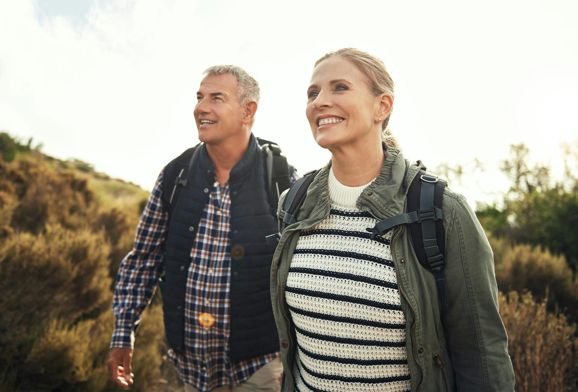smiling couple walking in the countryside with backpacks on