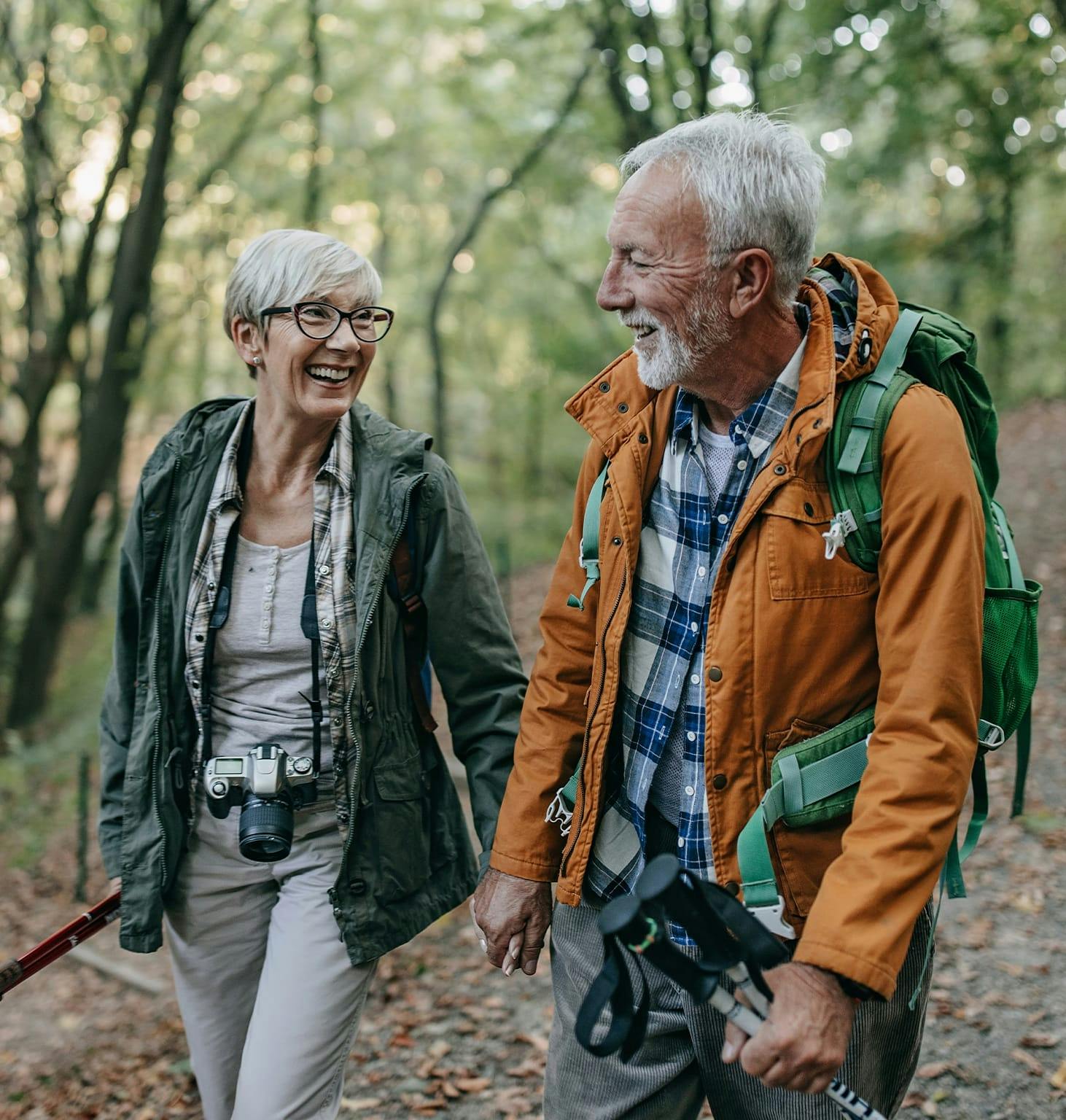 Older couple walking in the woods together with a backpack and a camera