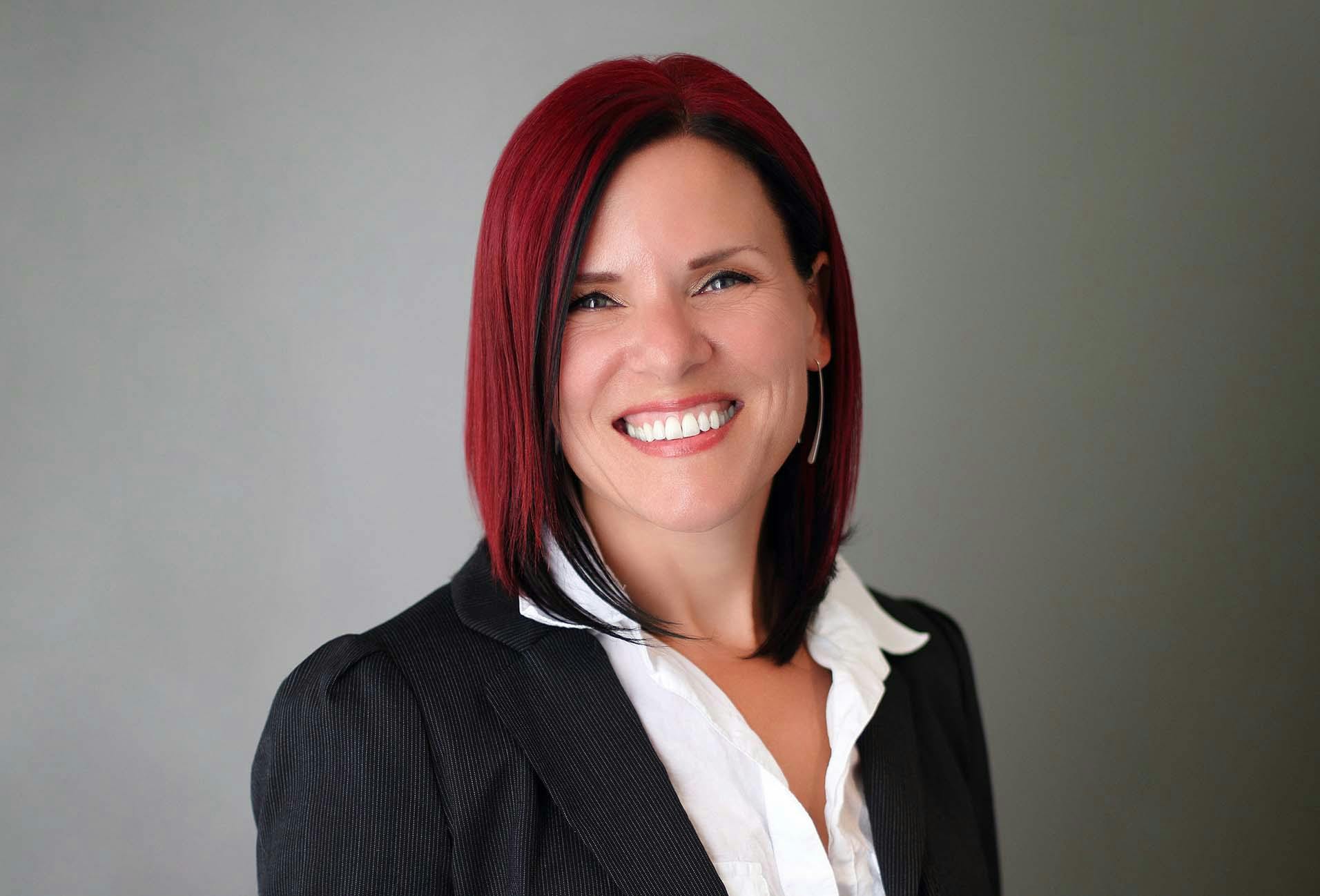 Dr. Lucy Hostetter in a black suit and white shirt with red hair