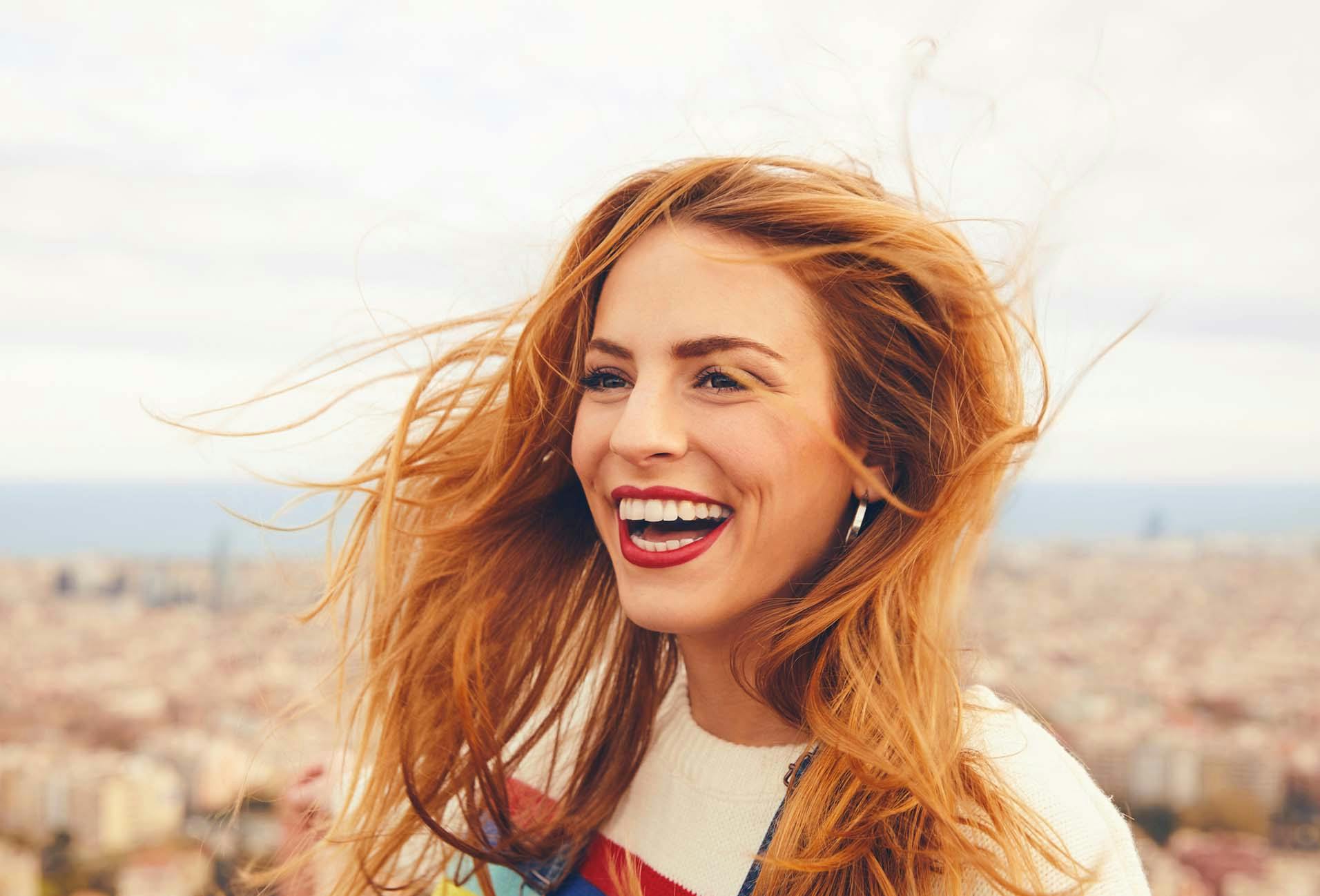 smiling woman with red hair and earphones on top of a building