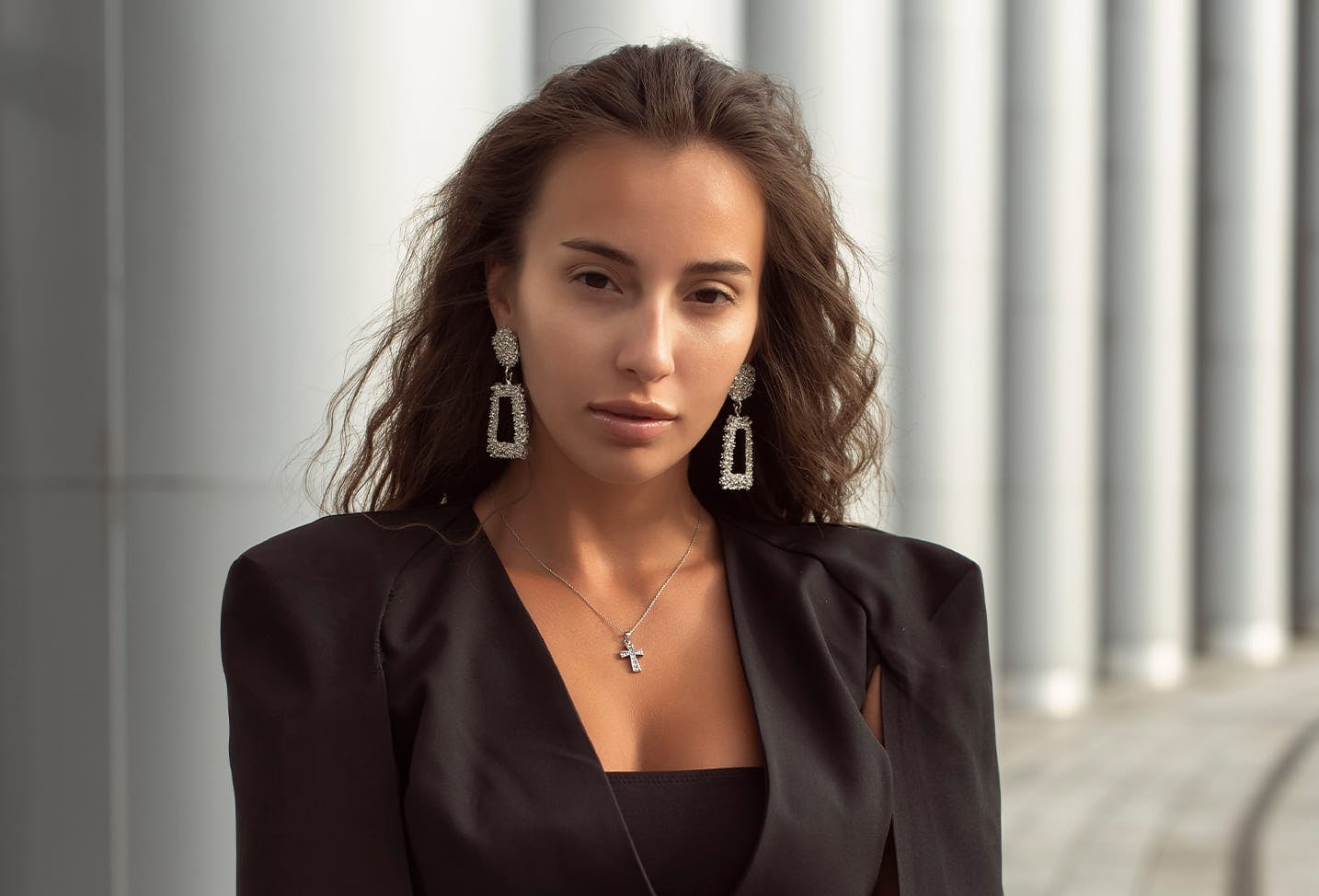 a woman with brunette hair in a black suit with large silver earrings