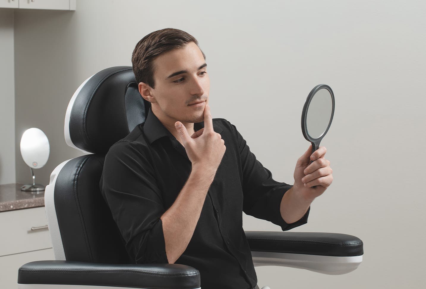 a male patient looking in mirror at a spot on his face