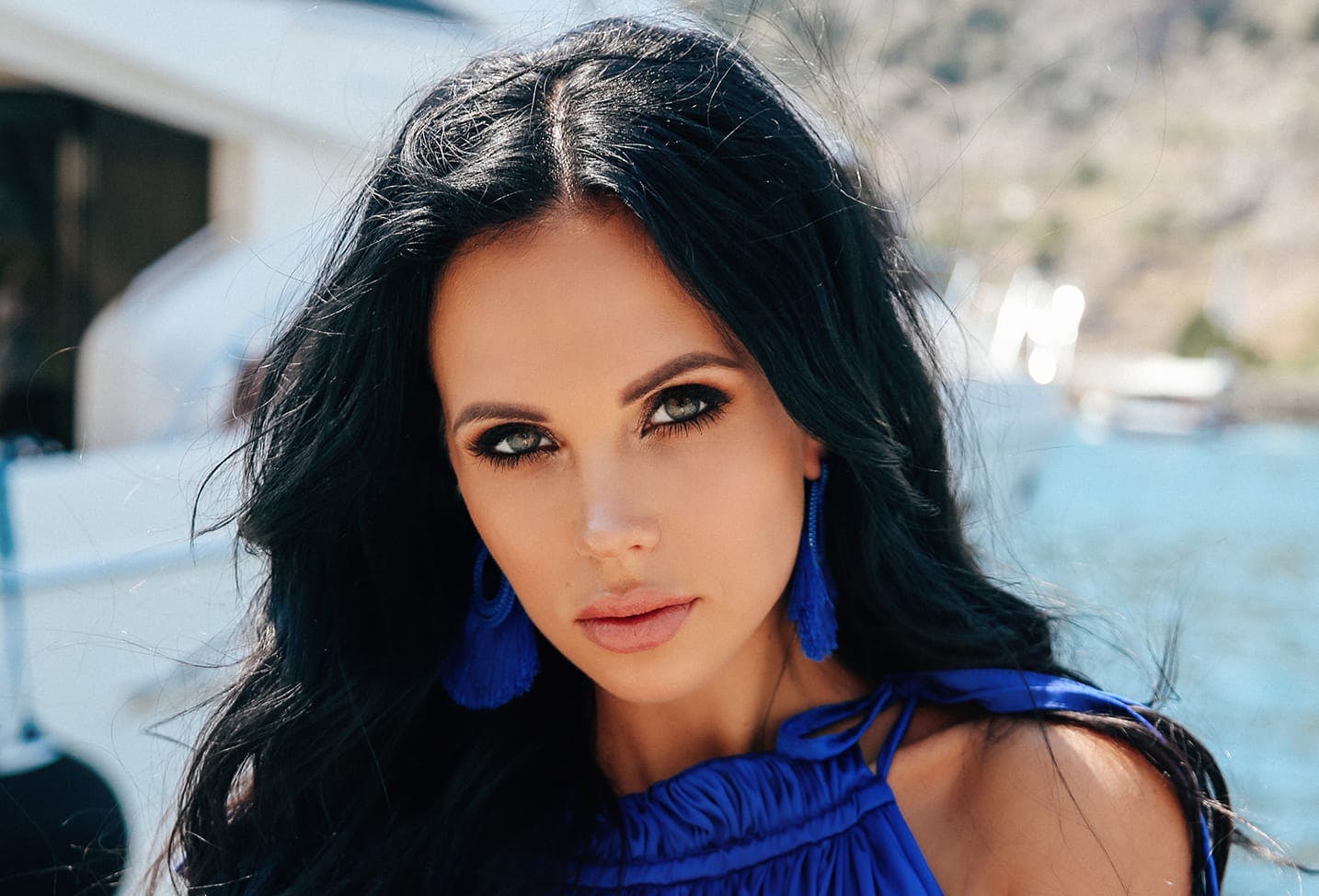 woman with black hair wearing a bright royal blue top and earrings
